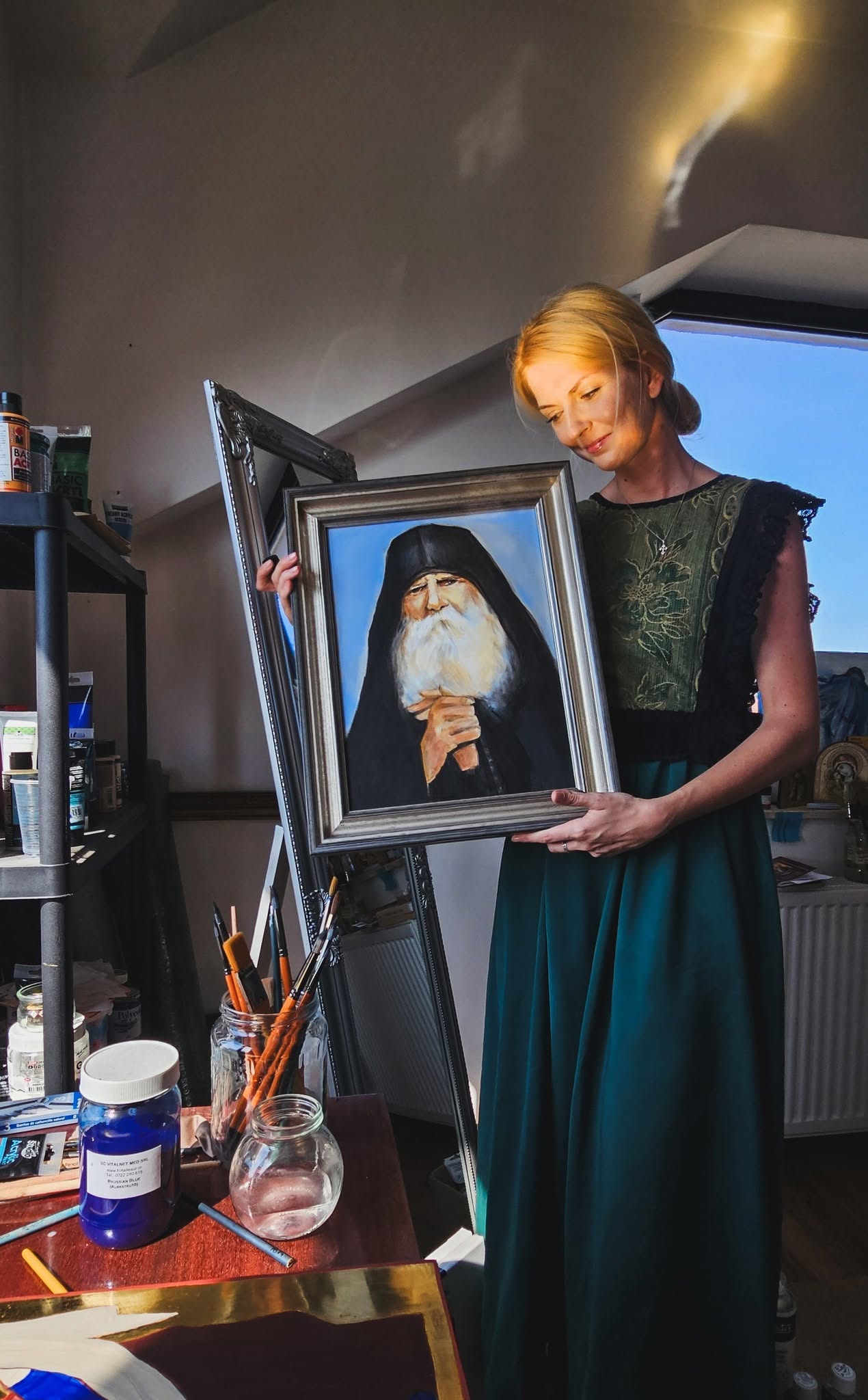 Anita M. Frâncu holding a framed portrait of a spiritual father in her studio.
