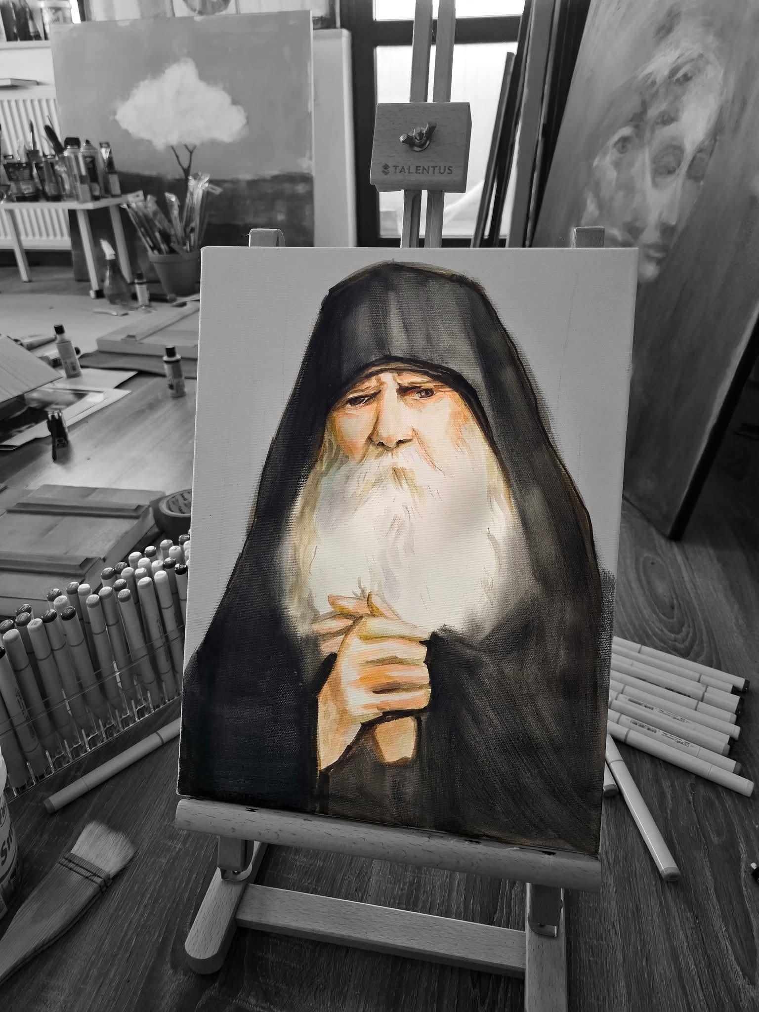 A portrait of a spiritual father on a small easel, among art materials and other paintings.