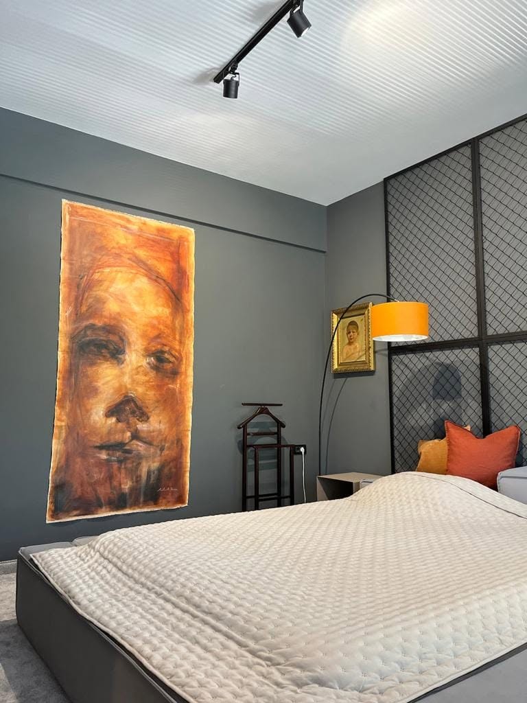 A portrait in warm tones displayed above a bed on a grey wall.