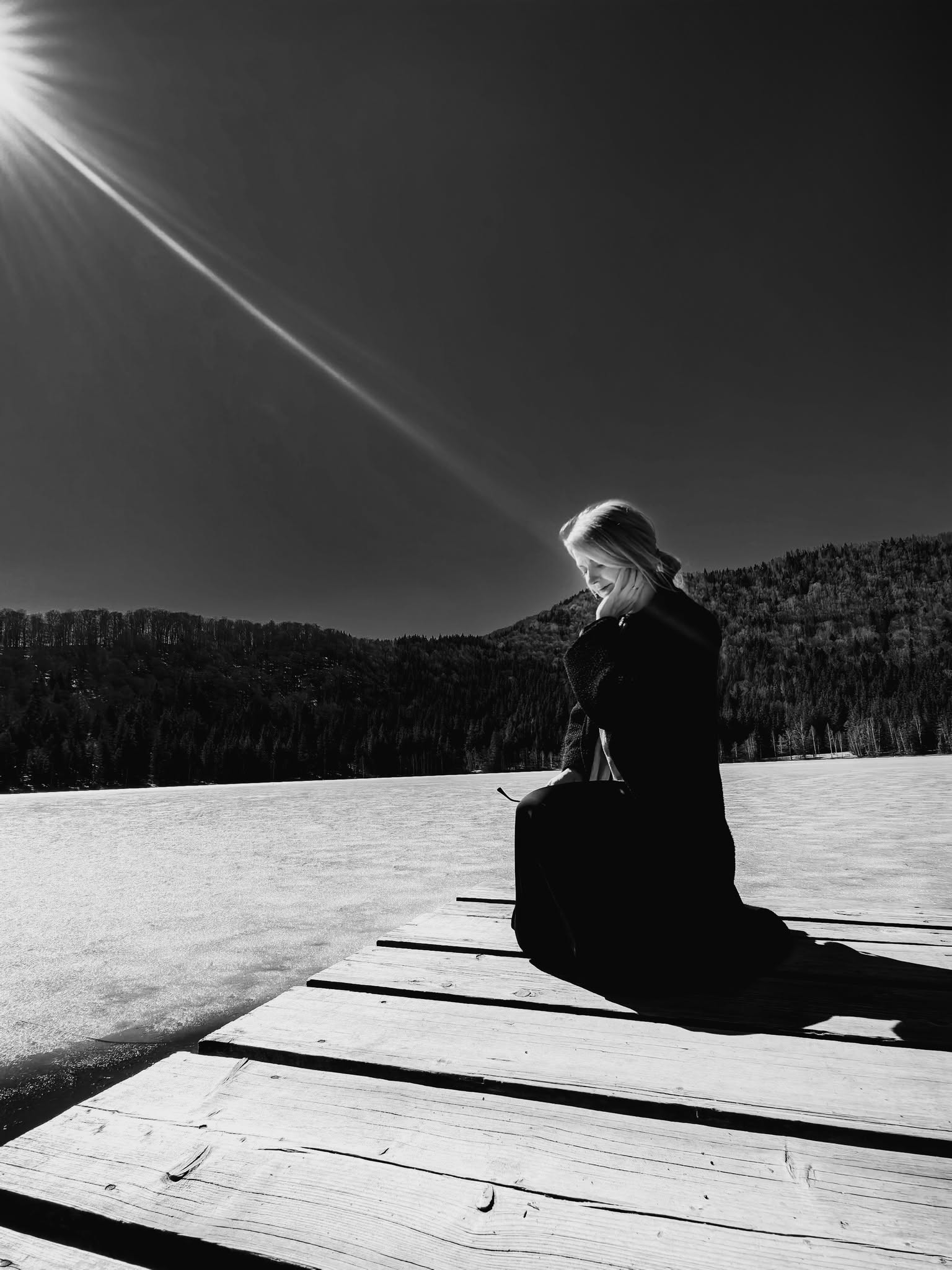 Black-and-white photograph of the artist seated beside a lake in a winter landscape.