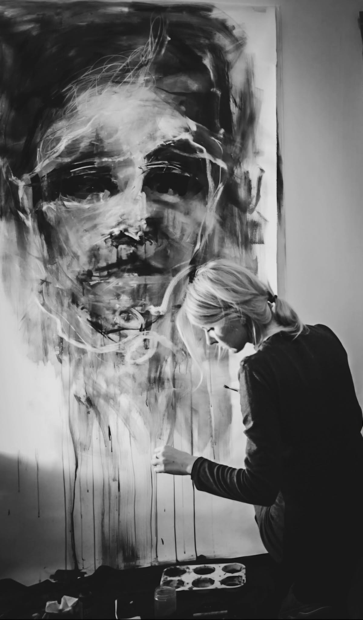 Anita M. Frâncu painting in her studio in front of a large portrait.