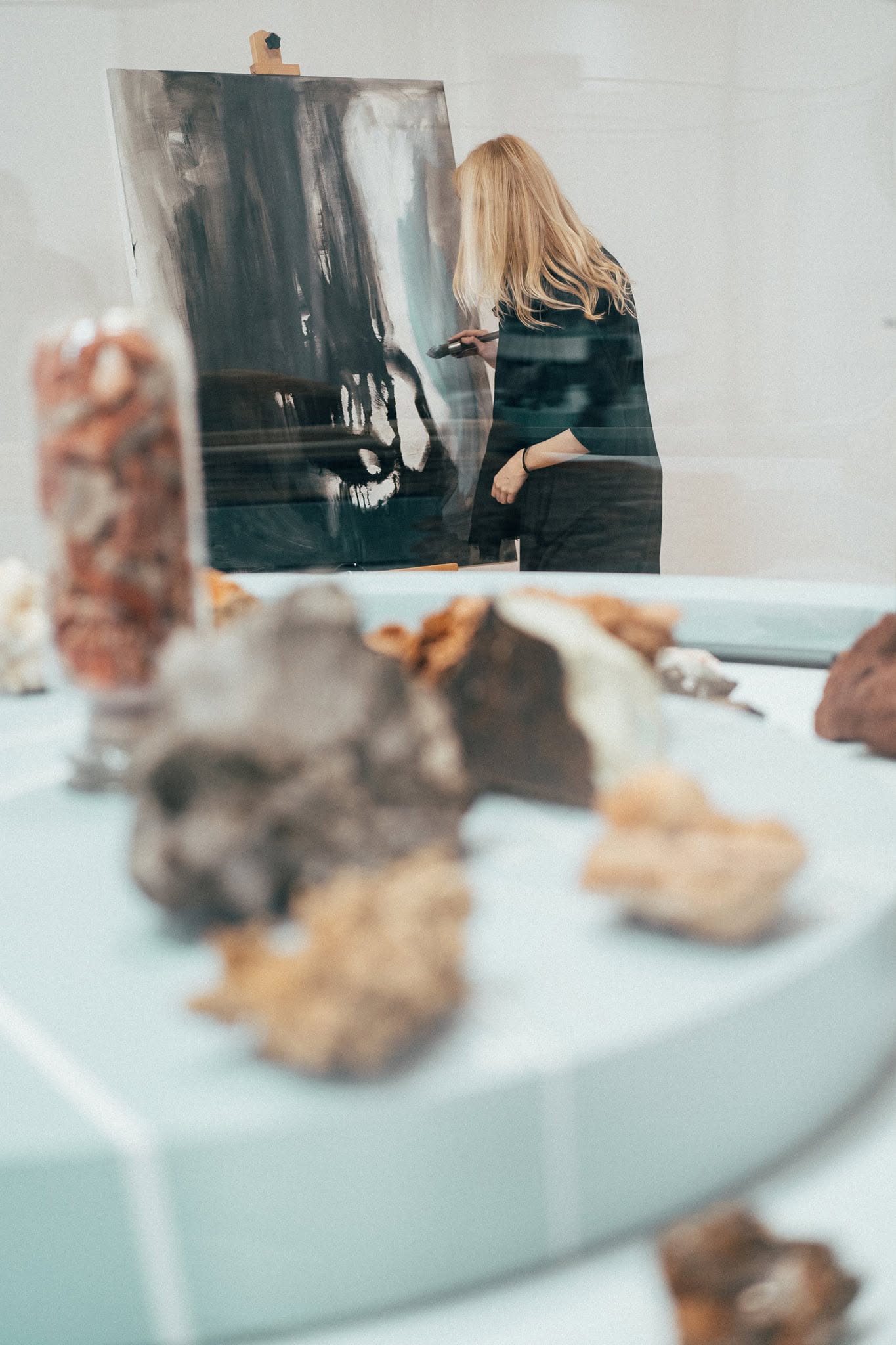 Anita Frâncu working on a canvas, photographed through a museum display case.