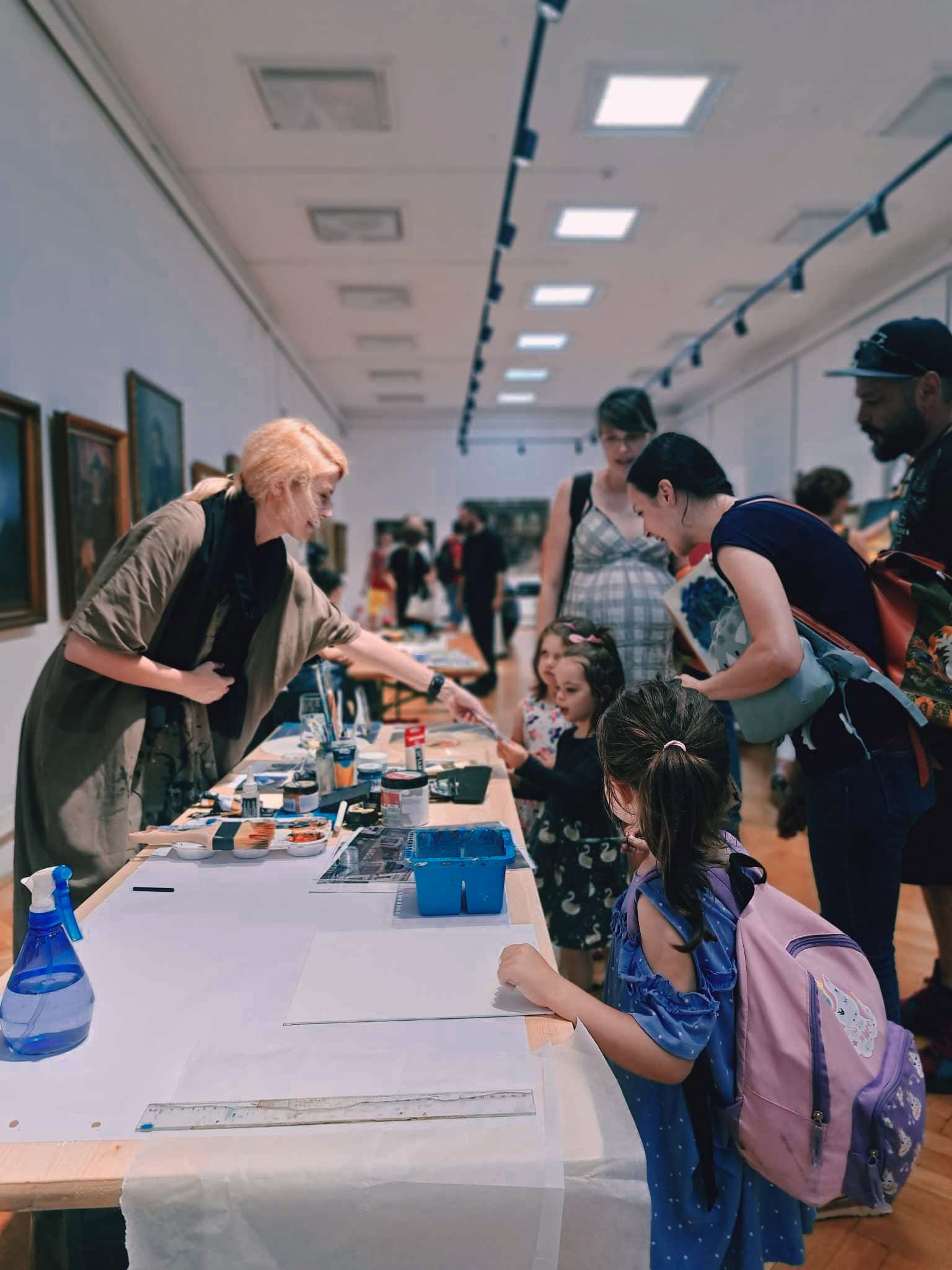 The artist talking with visitors of different ages beside a table of painting materials in the museum.